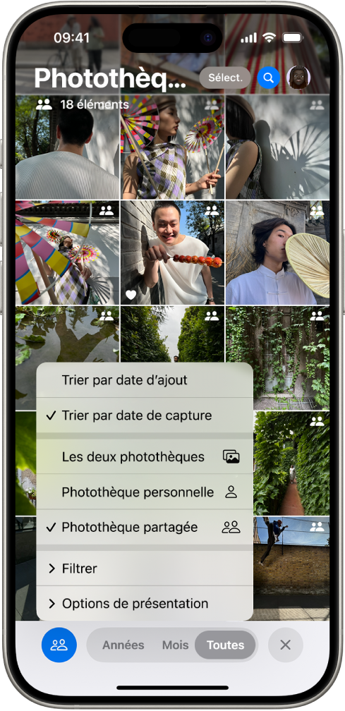 Une photothèque partagée iCloud dans l’app Photos. Le bouton « Photothèque partagée » dans le coin inférieur gauche est sélectionné, et la photothèque partagée est sélectionnée dans une liste d’options de photothèque. Toutes les photos affichées dans la photothèque possèdent une pastille dans le coin supérieur droit indiquant qu’elles appartiennent à une photothèque partagée.